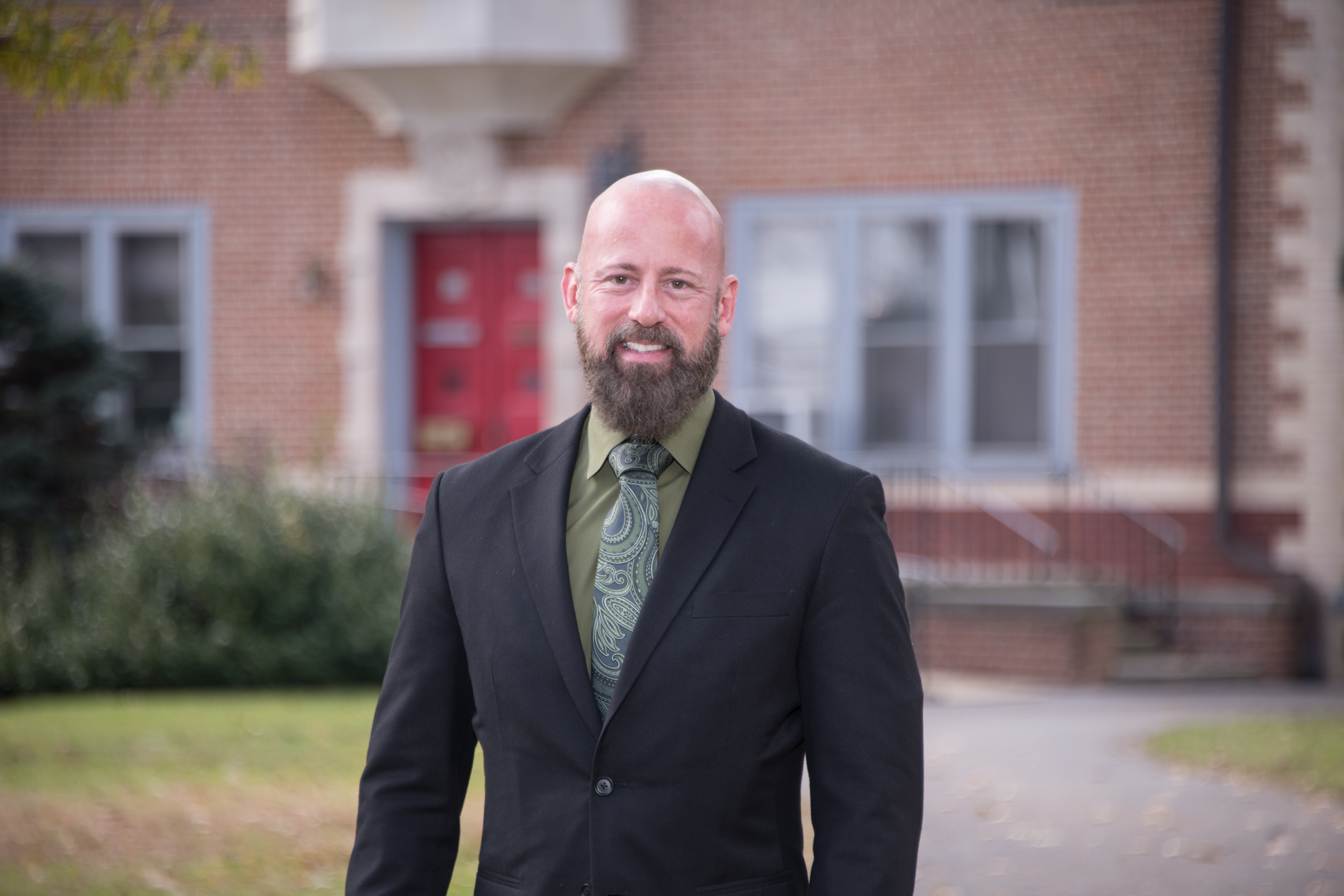 Man wearing black suit standing in front of Gabriel House on Muhlenberg College campus.